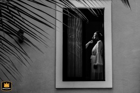 Tulum Colonial Suite, Mexico, provides the setting where a bride is elegantly framed by a sunlit window during her wedding preparations, viewed from the peaceful outdoor surroundings.